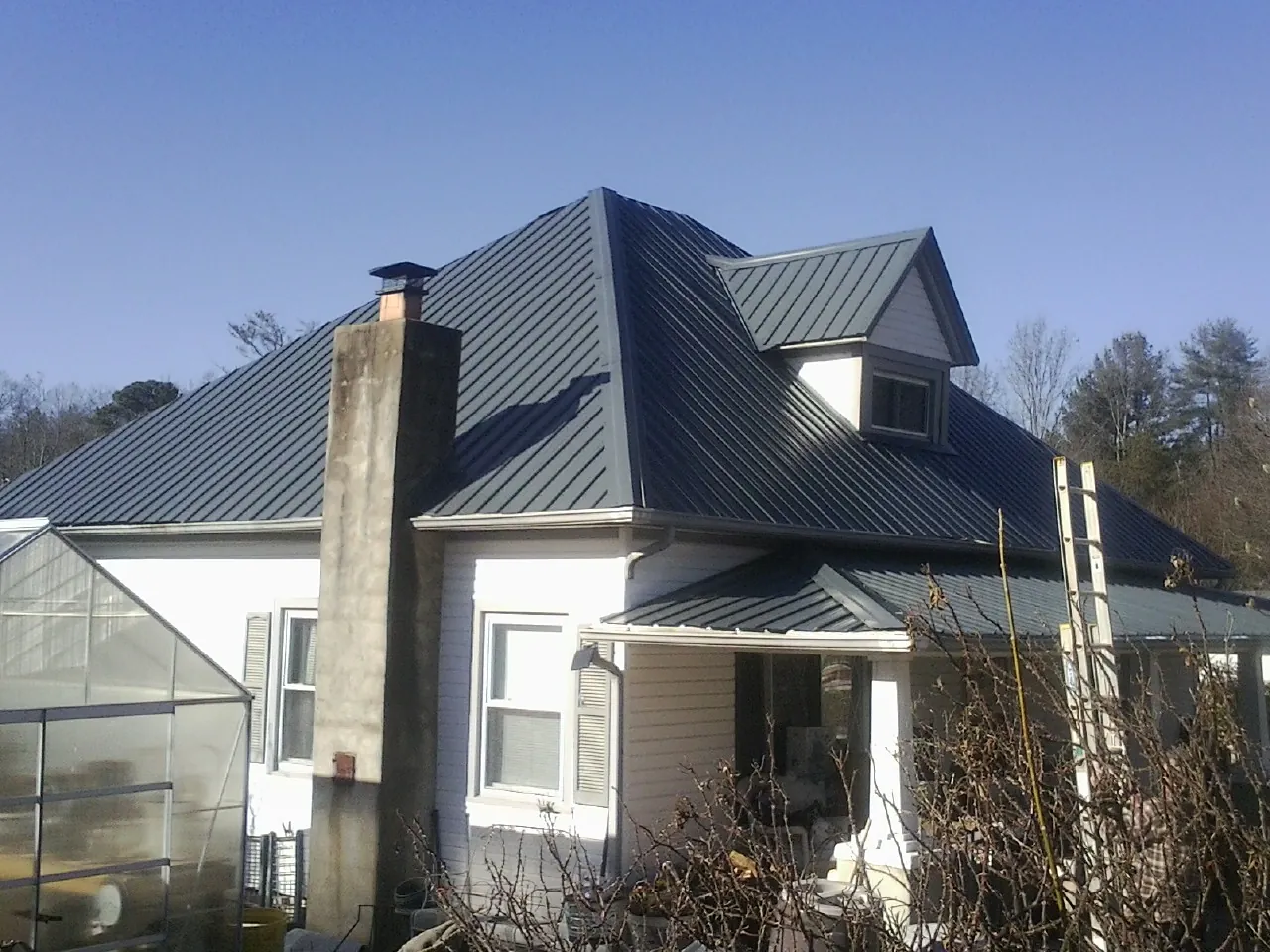 Dark blue standing seam metal roof on a white farmhouse with dormer — Slate & Tile Roof Repair by Roofing Brothers in North Bend