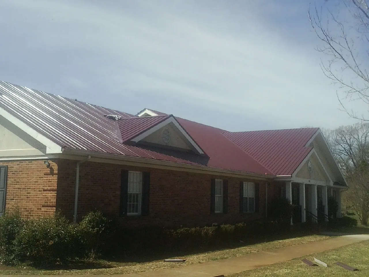 Red metal roof with gabled entries on a long brick building, from a Hail Damage Roof Repair job in North Bend