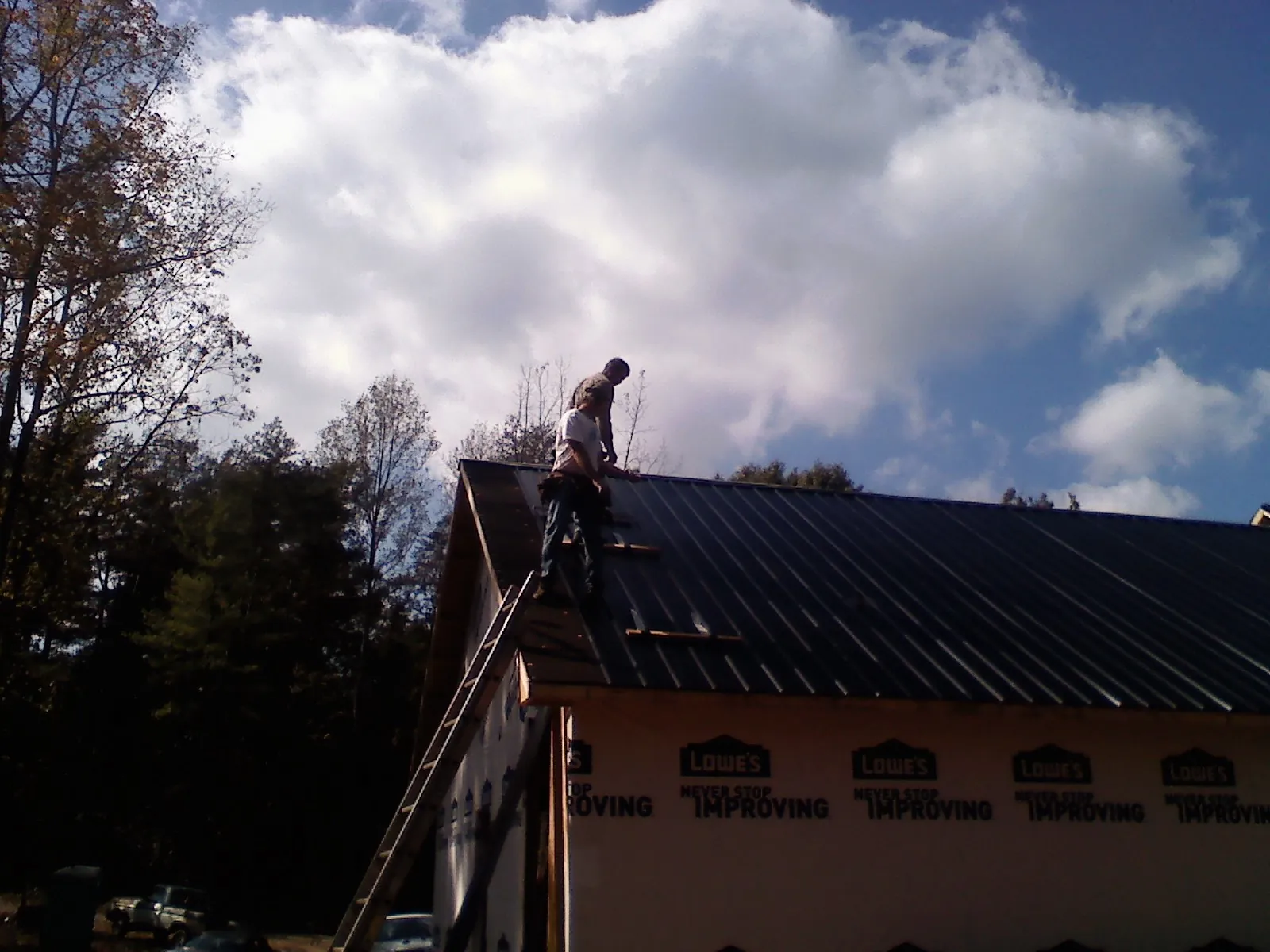 Roofer fastening dark metal panels high against a cloudy sky, from a Roof Inspection job in North Bend